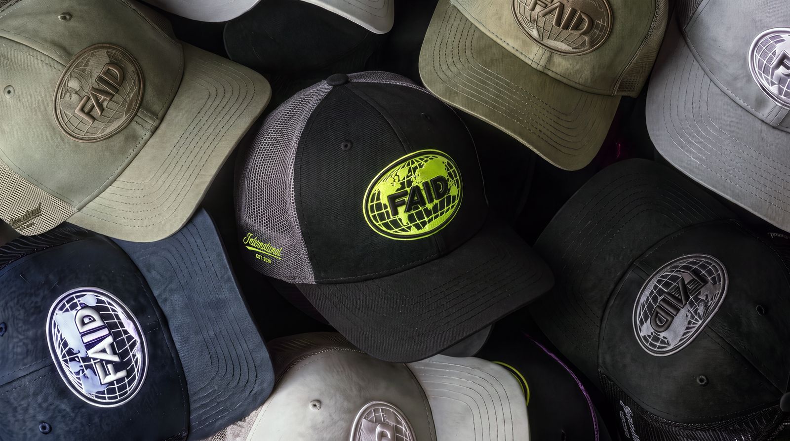 A pile of FAID Globe Trucker caps with the black and neon cap in the centre, surrounded by all black, all khaki, light grey and navy caps.
